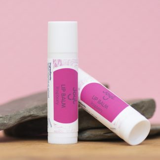 Two raspberry lip balms leaning against slate with a pink background.