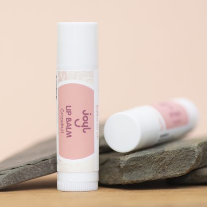 Two grapefruit lip balms leaning against slate with a pale pink background