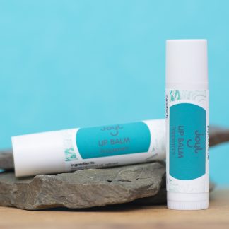 Two peppermint lip balms leaning against slate with a blue background